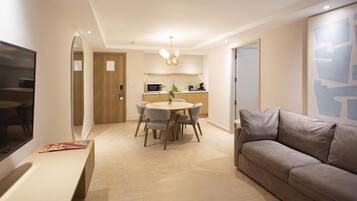 A modern living room with a sofa, a dining table with chairs, a kitchen area, and a TV mounted on the wall.