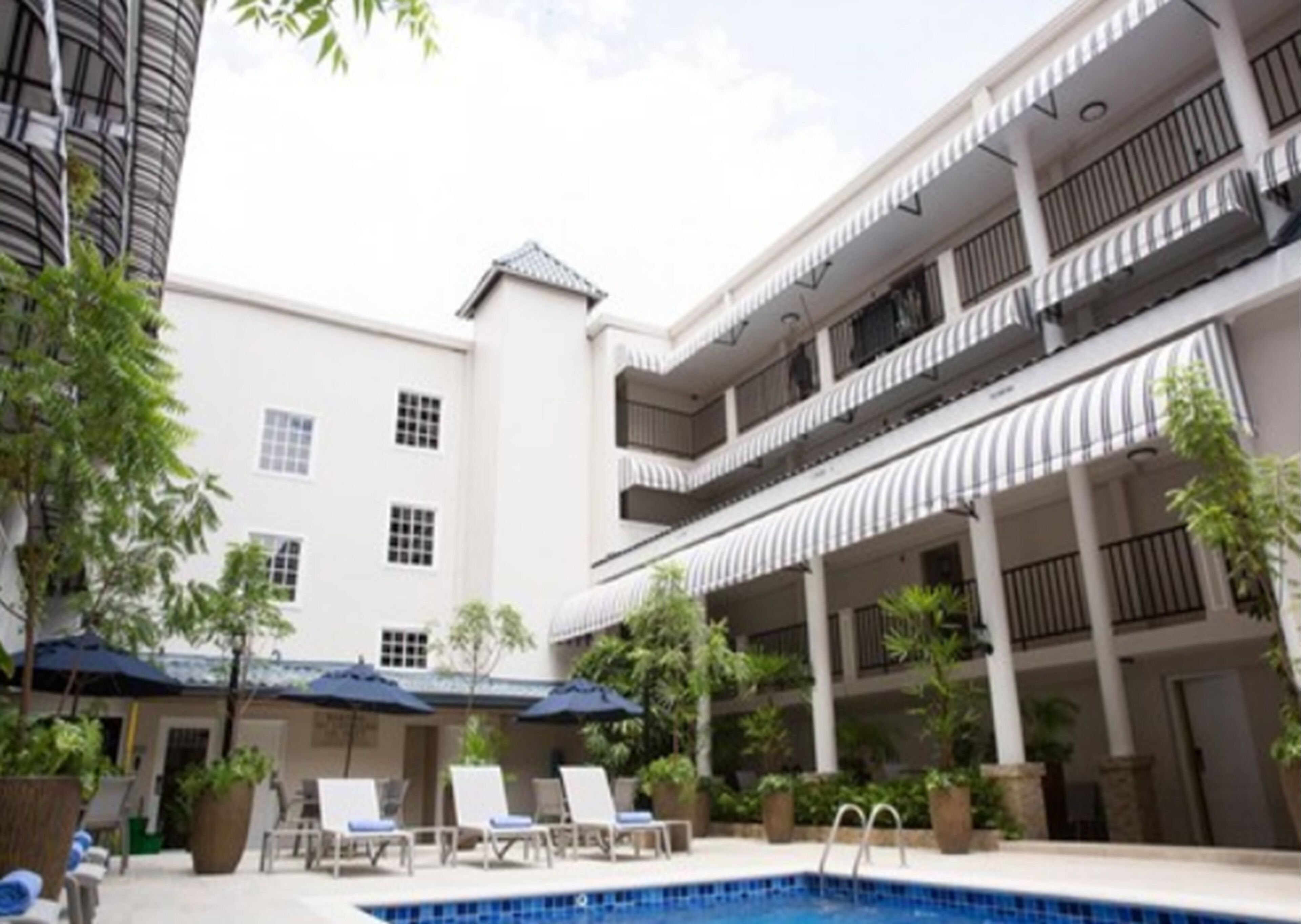 Pátio de hotel com piscina, espreguiçadeiras e guarda-sóis.