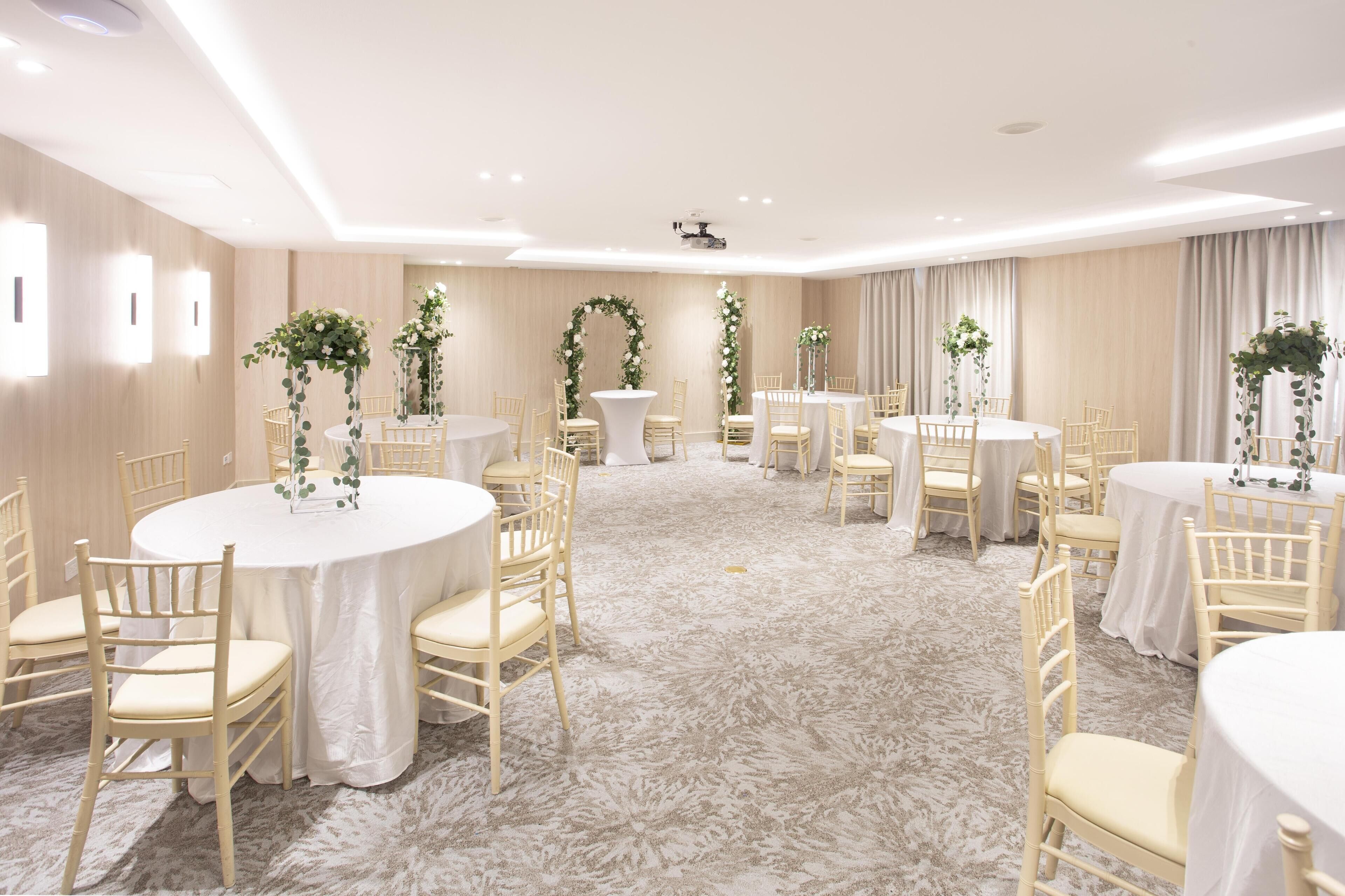 Un salón de conferencias con mesas redondas, sillas y decoración floral.
