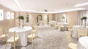 Un salón de conferencias con mesas redondas, sillas y decoración floral.