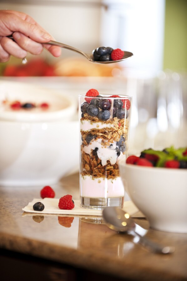 A layered dessert in a clear glass, with a spoon and berries on the side.