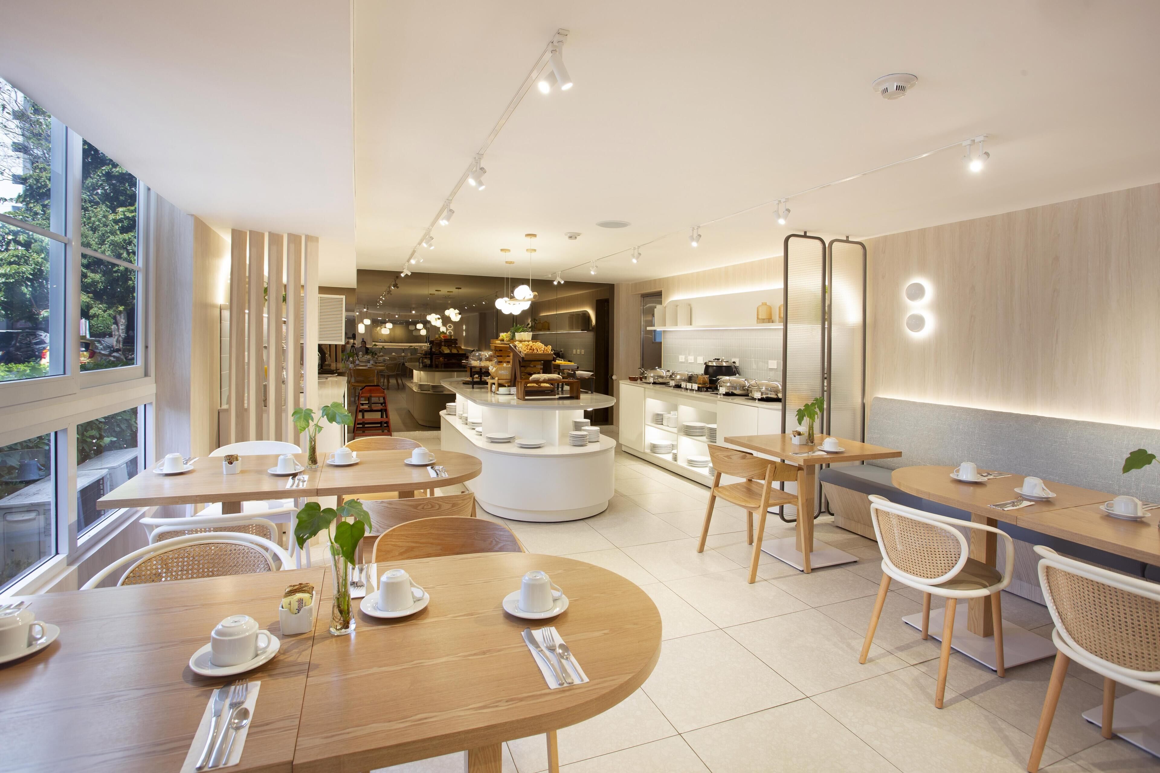 Un espace repas moderne avec des tables rondes, des chaises blanches et un îlot central doté d’un coin café.
