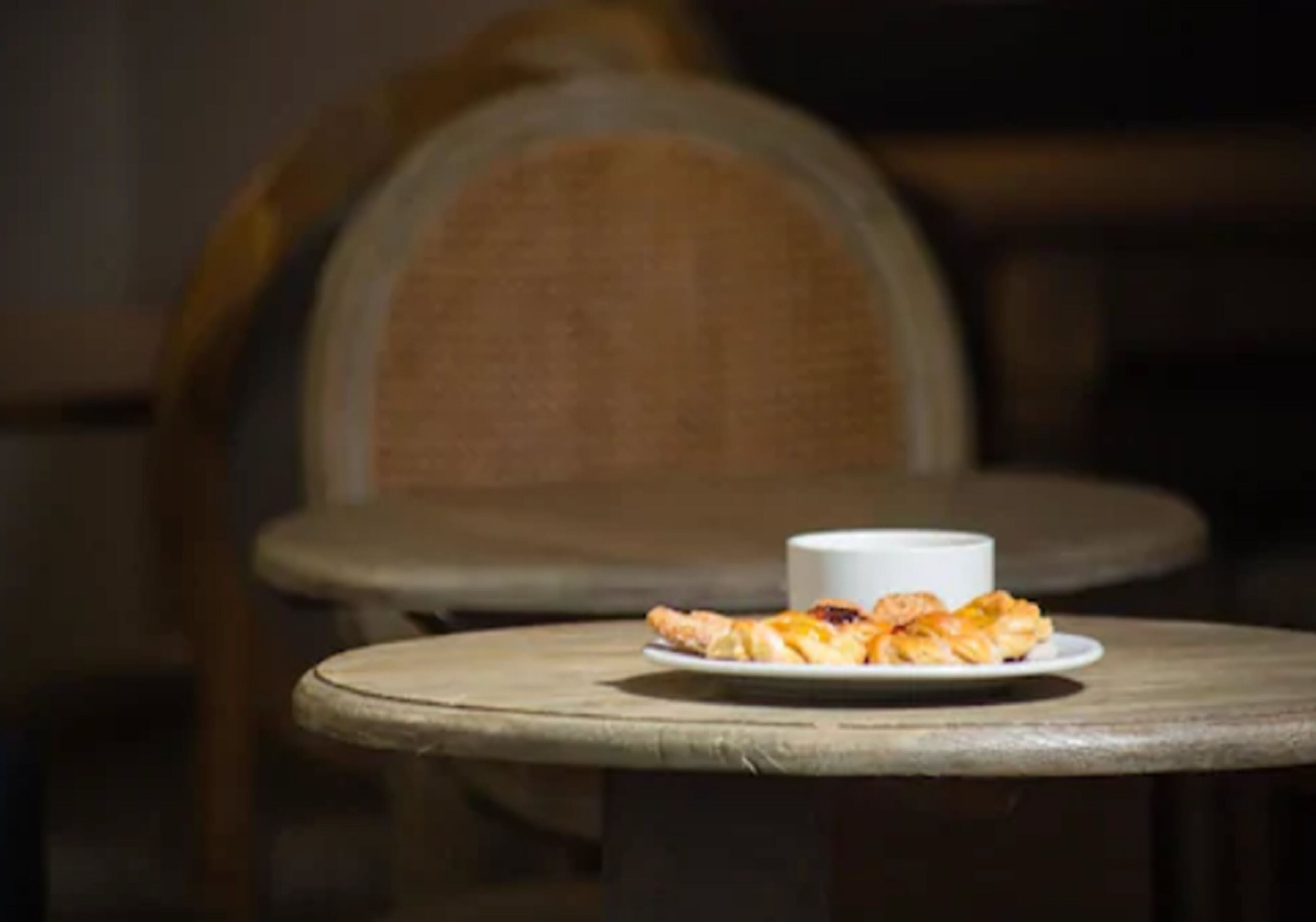 Une table avec une assiette de nourriture et une tasse, placée dans une pièce faiblement éclairée et meublée de meubles en bois.
