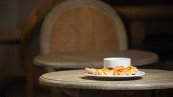 Une table avec une assiette de nourriture et une tasse, placée dans une pièce faiblement éclairée et meublée de meubles en bois.