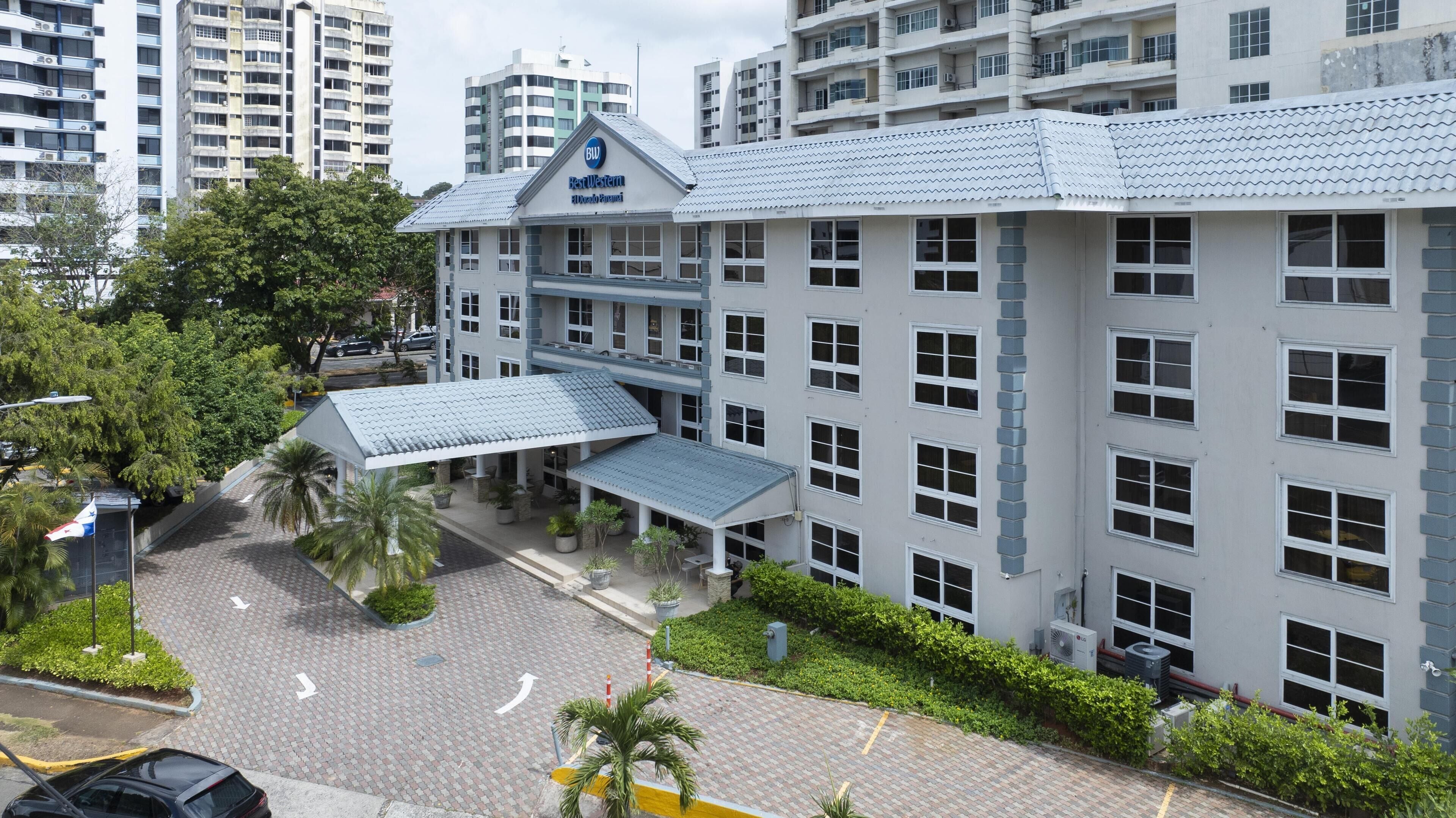 A hotel with a covered entrance, multiple floors, and a parking area with palm trees.