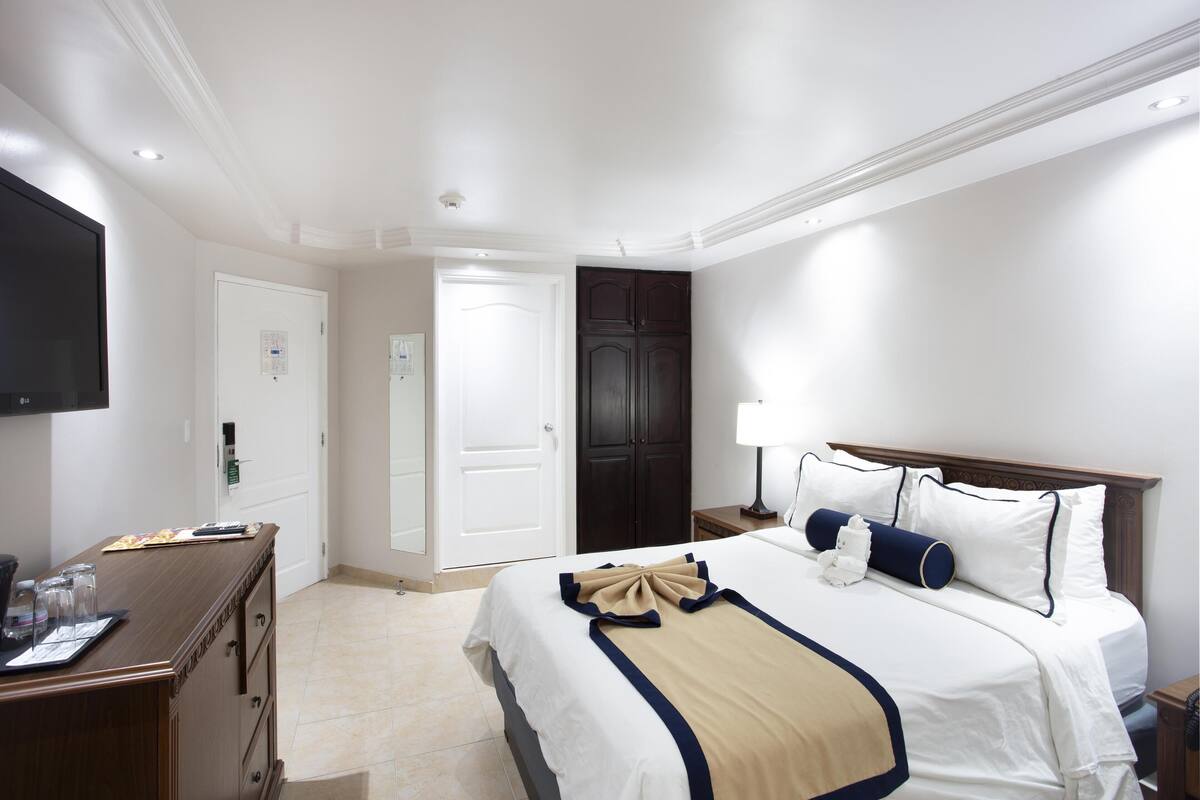 A hotel room with a bed, a desk with a computer, a TV, and a wardrobe.