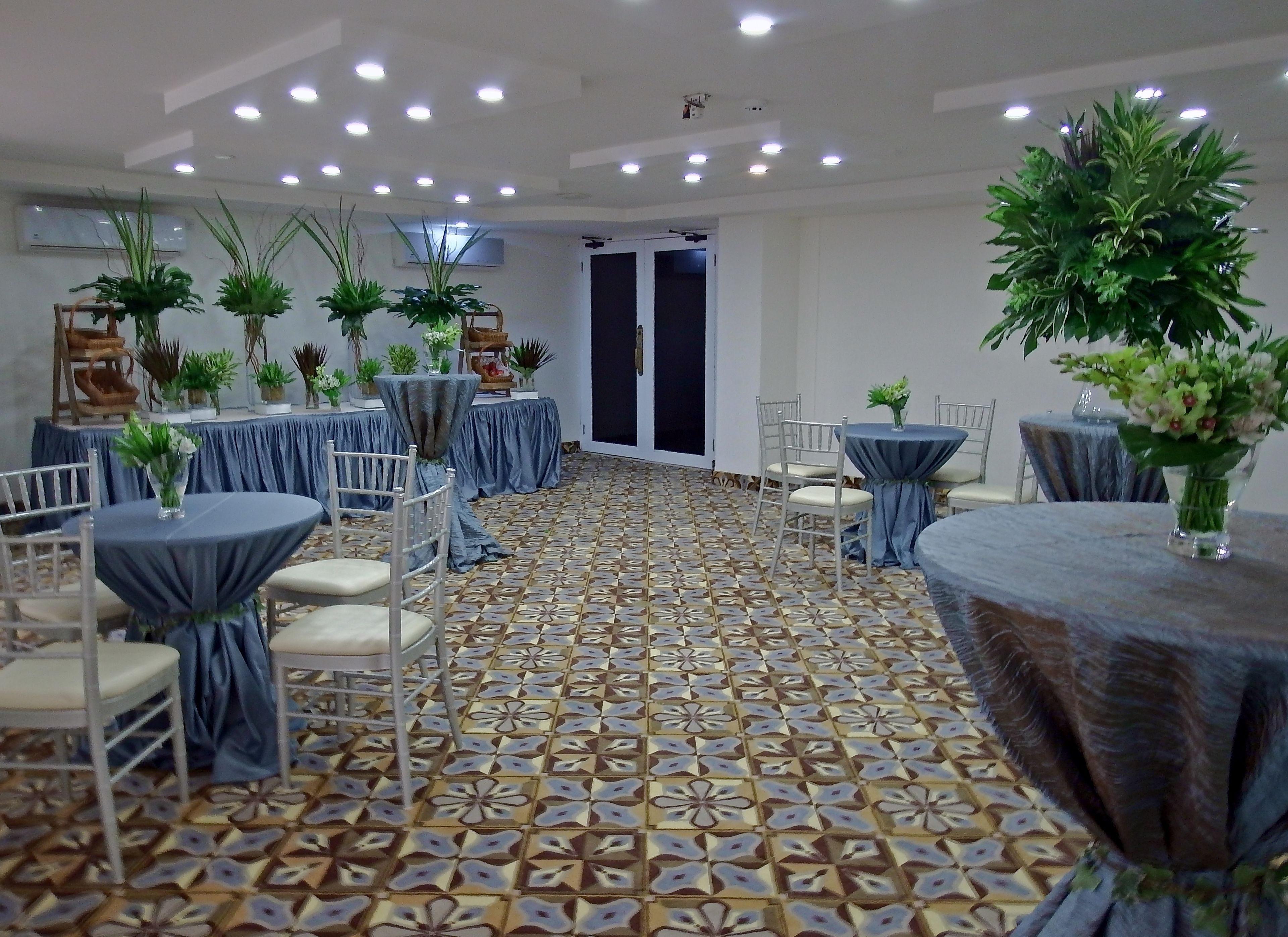 Una sala de banquets amb taules rodones cobertes amb camases blaves, cadires blanques i plantes en testos.