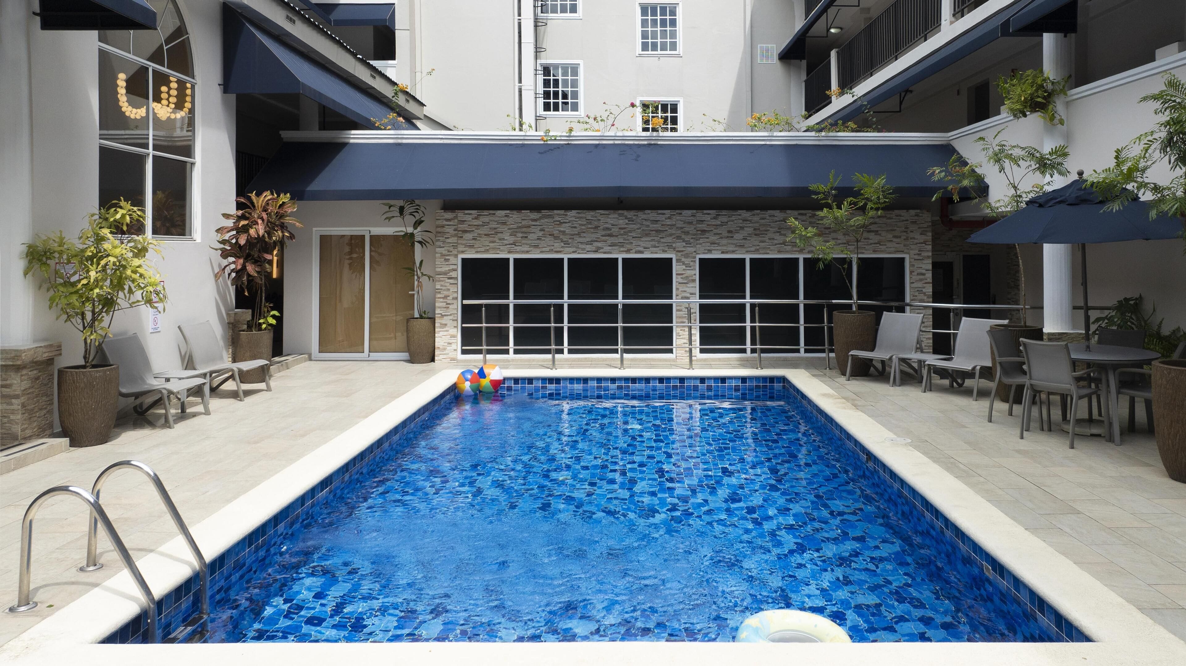 A swimming pool with a tiled edge, surrounded by lounge chairs and potted plants.