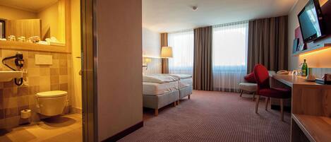 A hotel room with a bathroom, a bed, a desk, a chair, and a television.