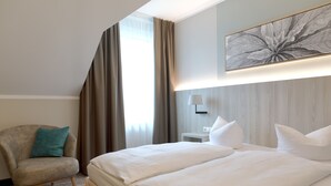 Habitació d'hotel amb un llit gran, una cadira, una làmpada i una obra d'art penjada a la paret.