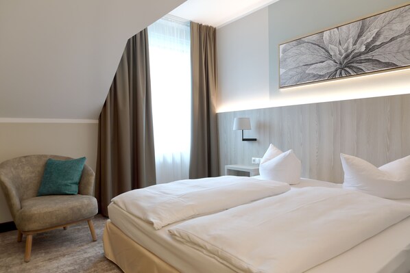 Una habitación de hotel con una cama grande, una silla, una lámpara y una obra de arte en la pared.
