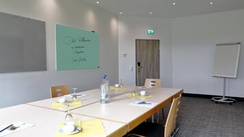 Une salle de conférence avec une longue table, des chaises, un tableau blanc et une porte portant un panneau indiquant la sortie de secours.