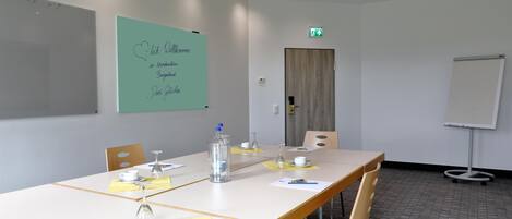 A conference room with a long table, chairs, a whiteboard, and a door with an emergency exit sign.