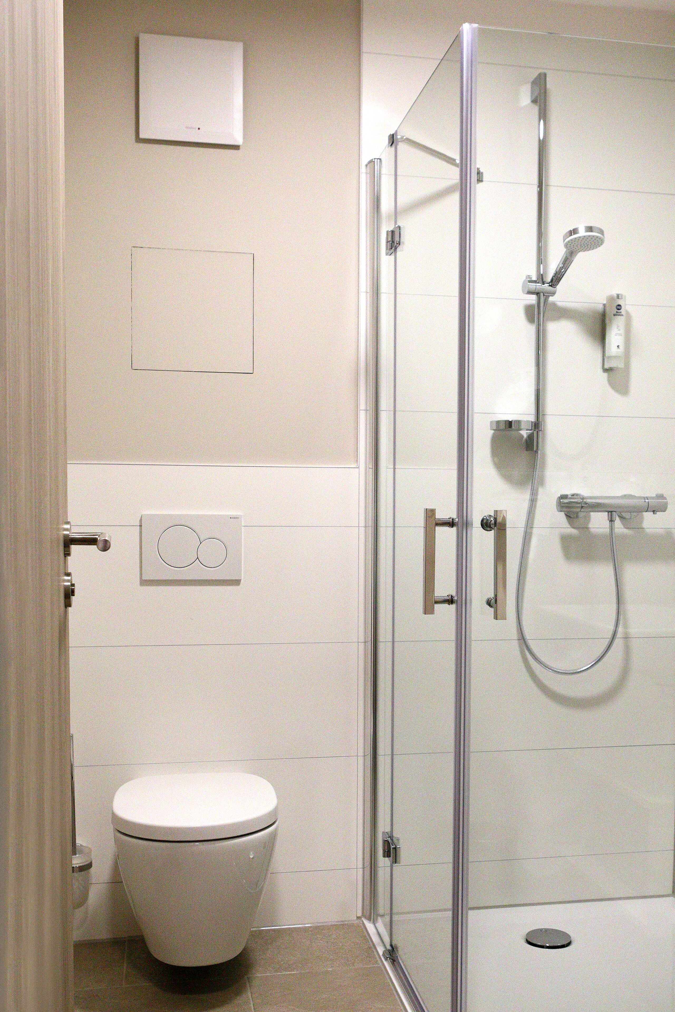 Un baño con inodoro, ducha con mampara de vidrio y panel de control en la pared.