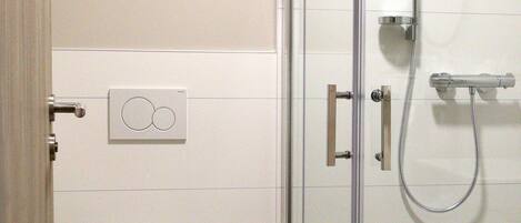 Un baño con inodoro, ducha con mampara de vidrio y panel de control en la pared.