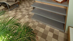 Un área de recepción con piso a cuadros, zona de descanso con sillones acolchados, un mostrador de recepción y vista a un jardín a través de una ventana.