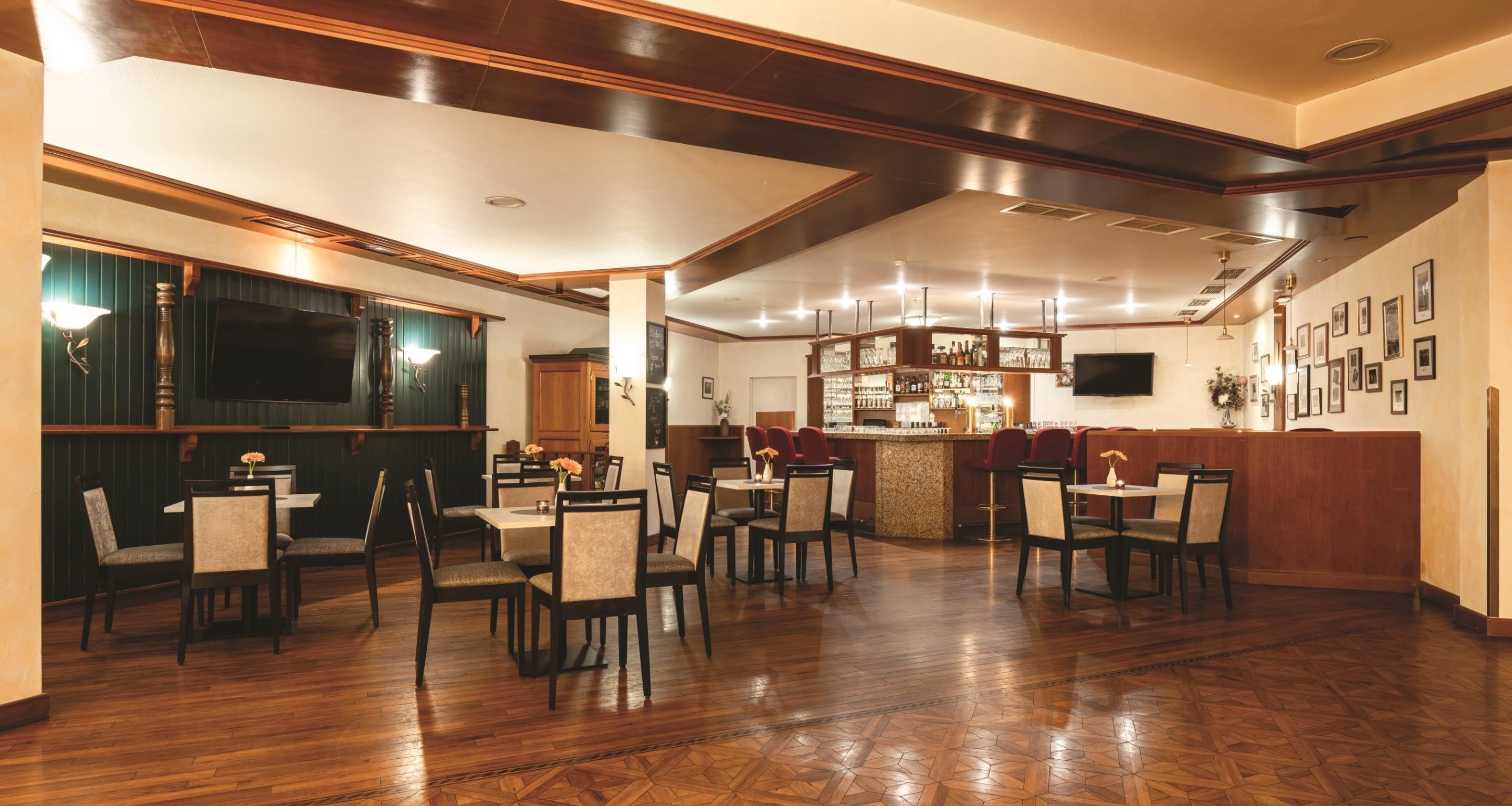 Un comedor amplio con suelo de madera, varias mesas y sillas. Cuenta con una zona de bar con mostrador y estantes llenos de botellas.