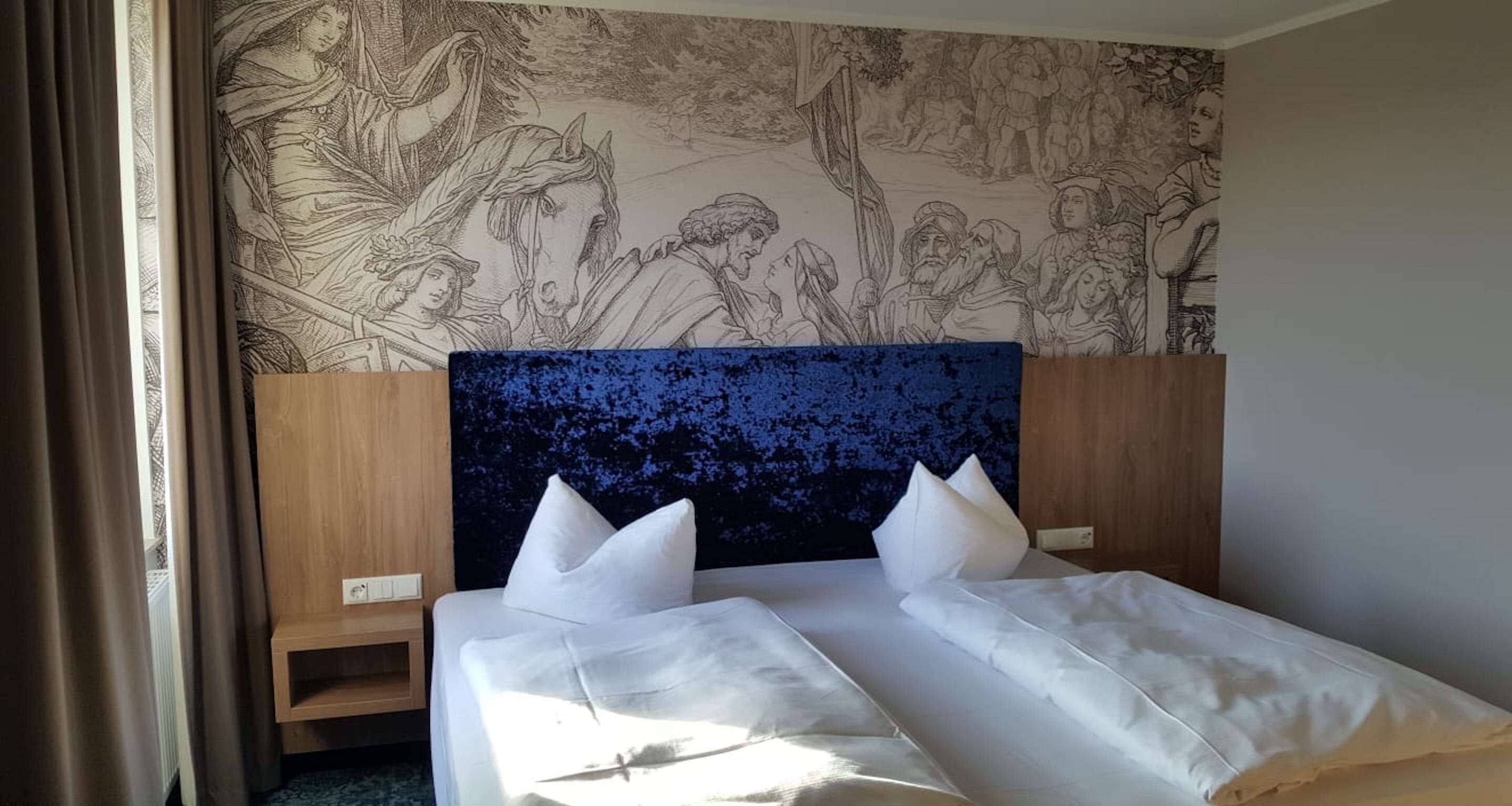 Une chambre d’hôtel avec un grand lit, deux oreillers, une tête de lit en bois et une fresque murale.
