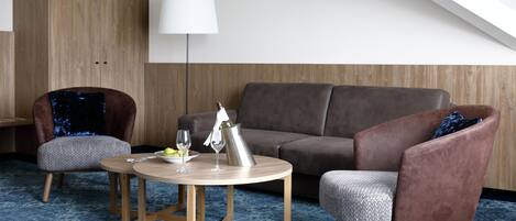 Un salon moderne avec un canapé marron, deux fauteuils, une petite table en bois et un lampadaire.