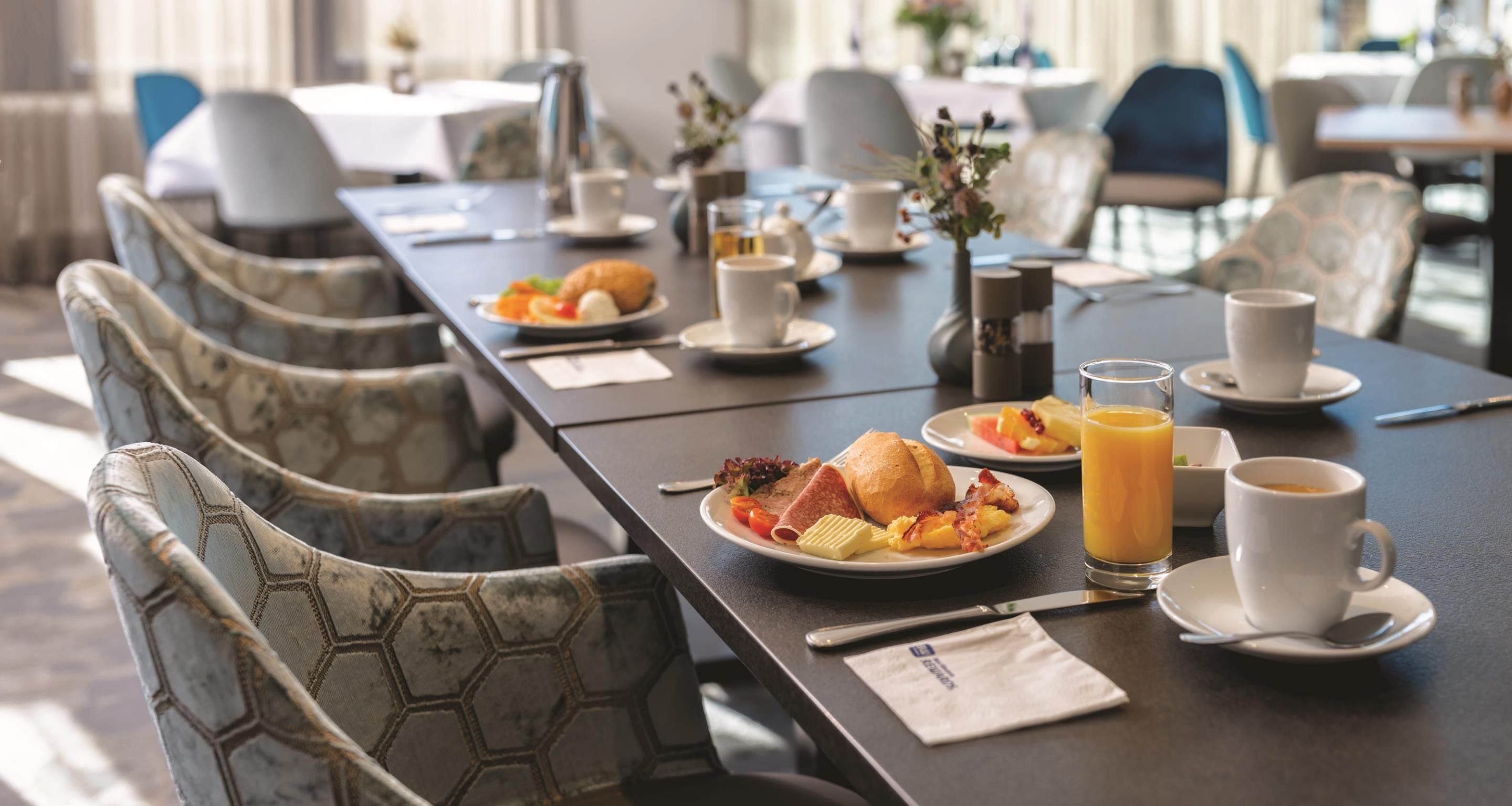 Desayuno servido con una mesa para dos, que incluye platos de comida, un vaso de jugo de naranja y una taza de café.