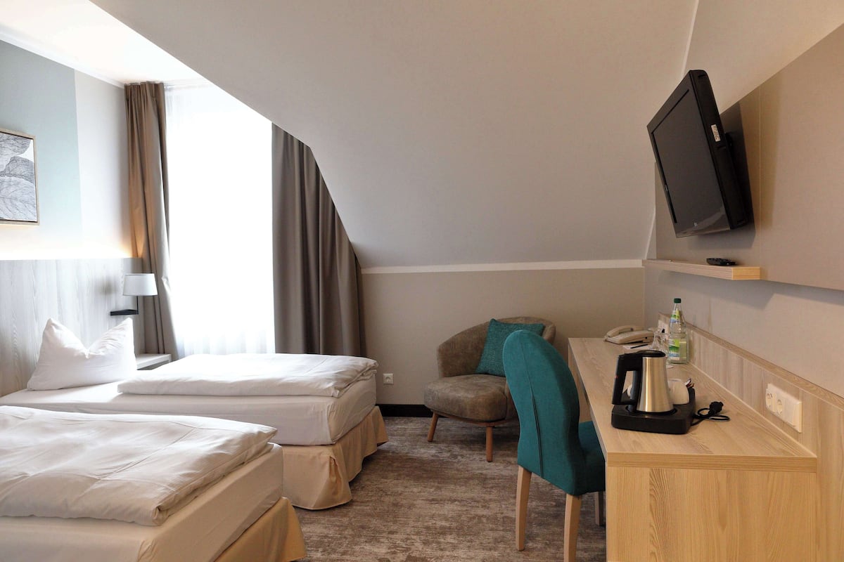 A hotel room with two beds, a desk with a coffee maker, a TV, and a chair.