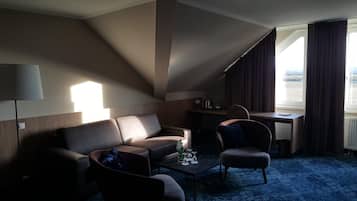 Une chambre d’hôtel avec un canapé, un fauteuil et une petite table sur laquelle se trouvent des verres et une bouteille.