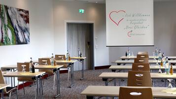 Ein Konferenzraum mit Tischen, Stühlen und einer Projektionsleinwand, auf der eine Begrüßungsnachricht angezeigt wird.