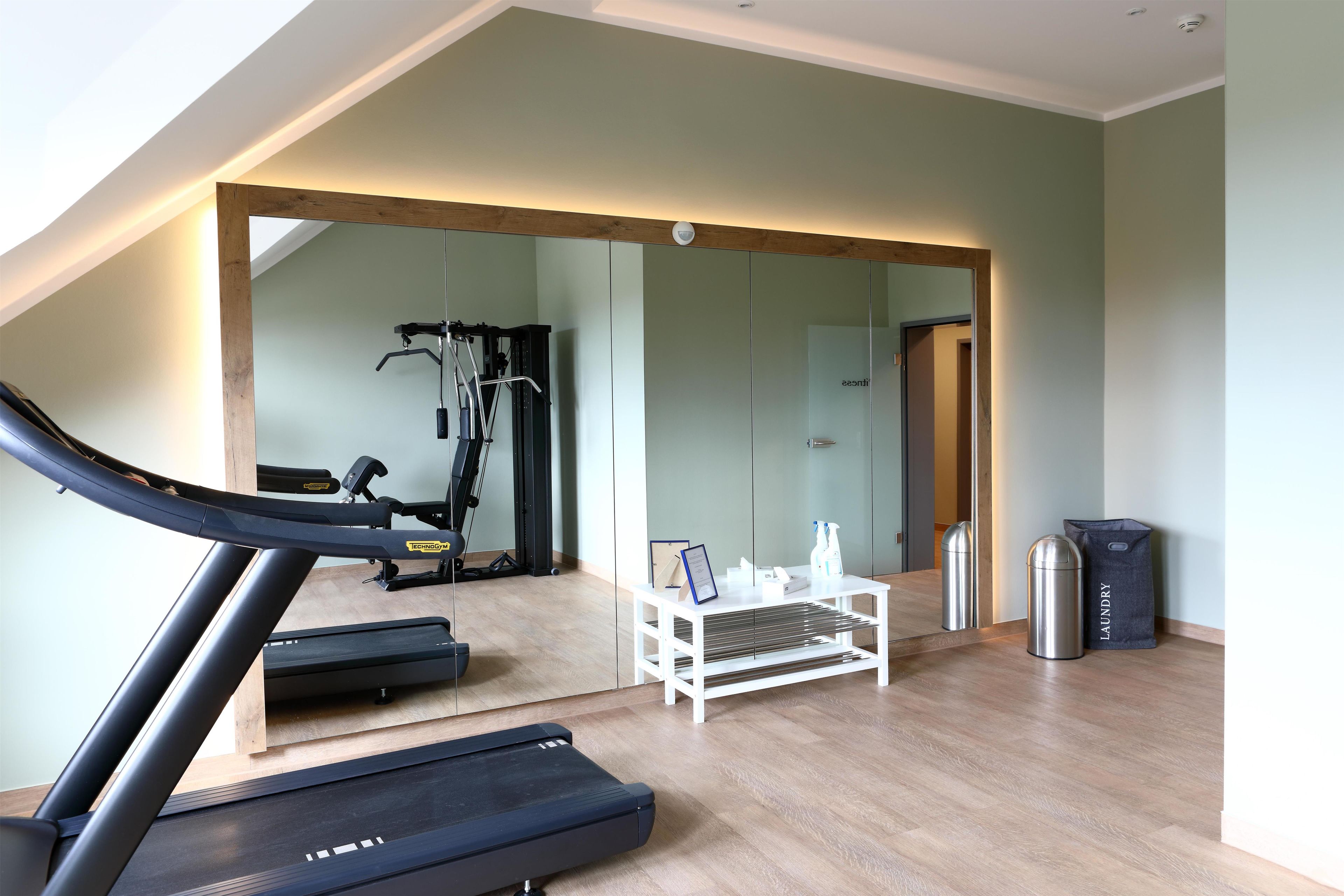 Un gimnasio en casa con cinta de correr, máquinas de pesas y un espejo que refleja el espacio.