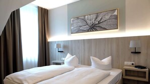 Una habitación de hotel con una cama grande, dos mesitas de noche, una lámpara de pared y una obra de arte enmarcada sobre la cama.