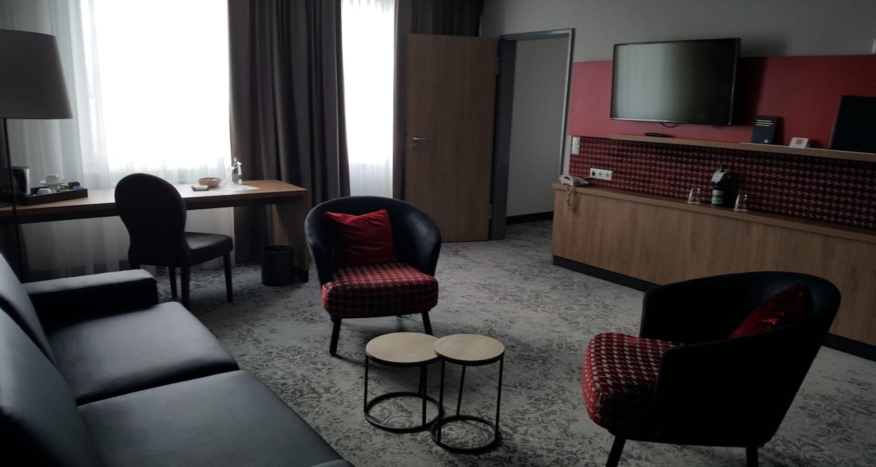 Une chambre d’hôtel comprenant un canapé, deux fauteuils, une petite table à manger, un téléviseur et un mini-bar.