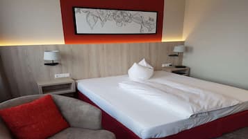 Ein Hotelzimmer mit einem Bett, einer roten Akzentwand, einer gerahmten Blumenblume, zwei Nachttischlampen und einem roten Kissen auf einem grauen Sessel.
