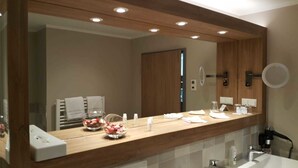 Un baño moderno con tocador de madera, un espejo grande y un cuenco de vidrio con flores.
