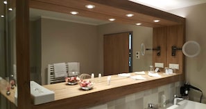 Un baño moderno con tocador de madera, un espejo grande y un cuenco de vidrio con flores.