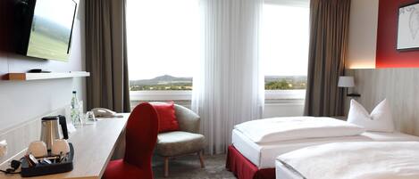 Habitación de hotel con escritorio, dos camas, televisión y vista al paisaje.