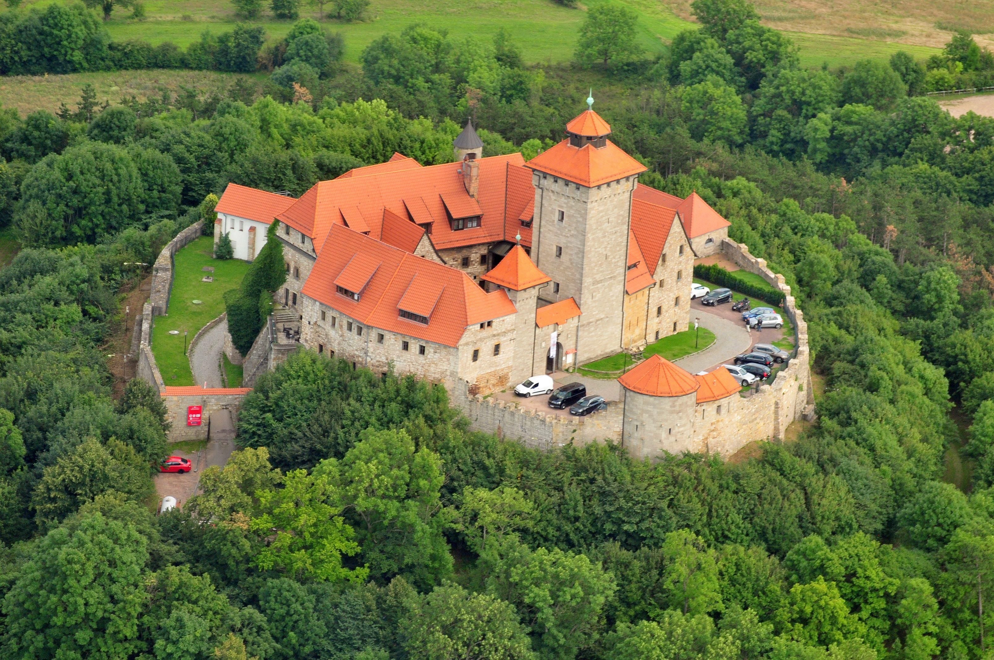 Eine Burg mit einem zentralen Turm, umgeben von einer Steinmauer und üppigem Grün.