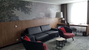 Una habitación de hotel moderna con un sofá de cuero negro, un sillón rojo y negro, una mesita redonda y un escritorio con una lámpara.