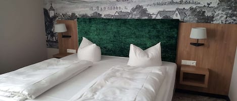 A neatly made bed with white linens and pillows, a green upholstered headboard, and two bedside tables with lamps.
