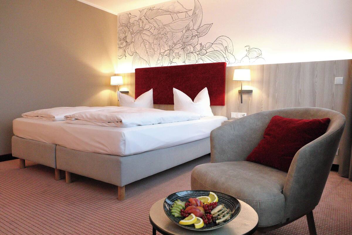 A hotel room with a bed, a chair, a fruit bowl, and a wall with a floral design.