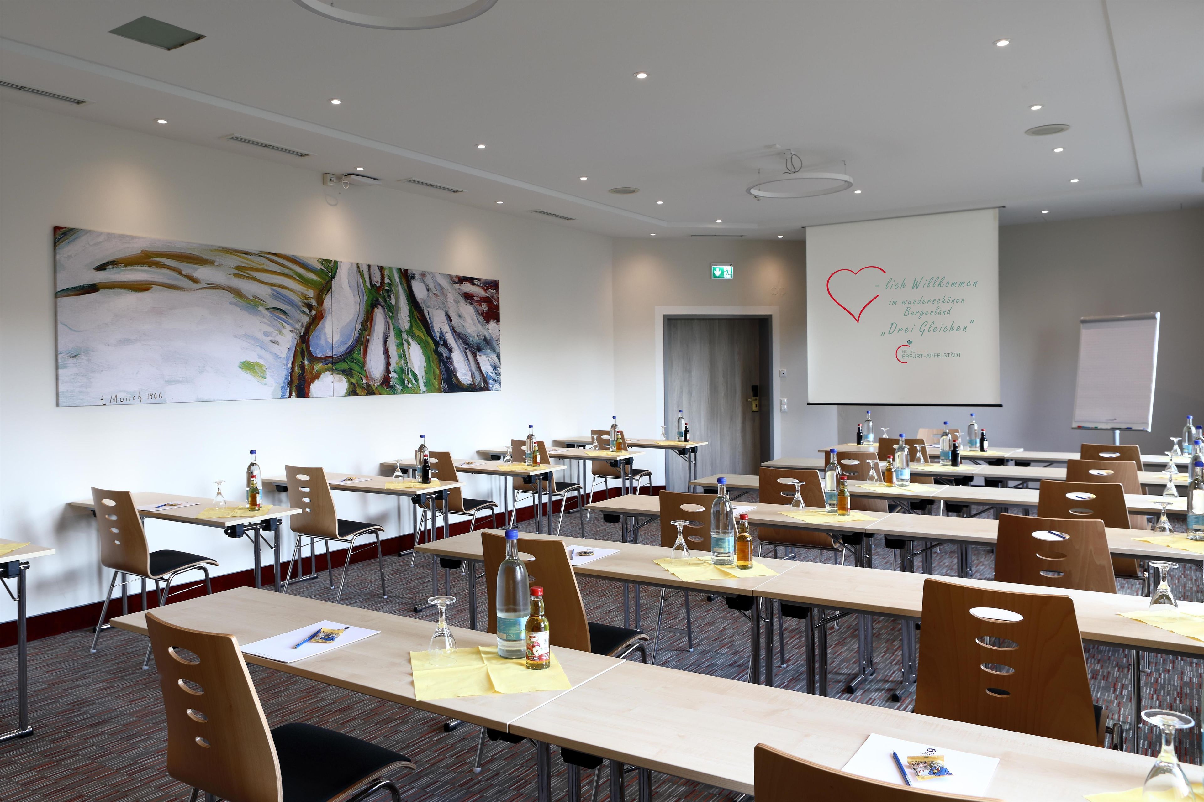 A conference room with multiple tables, chairs, and a large abstract painting on the wall.