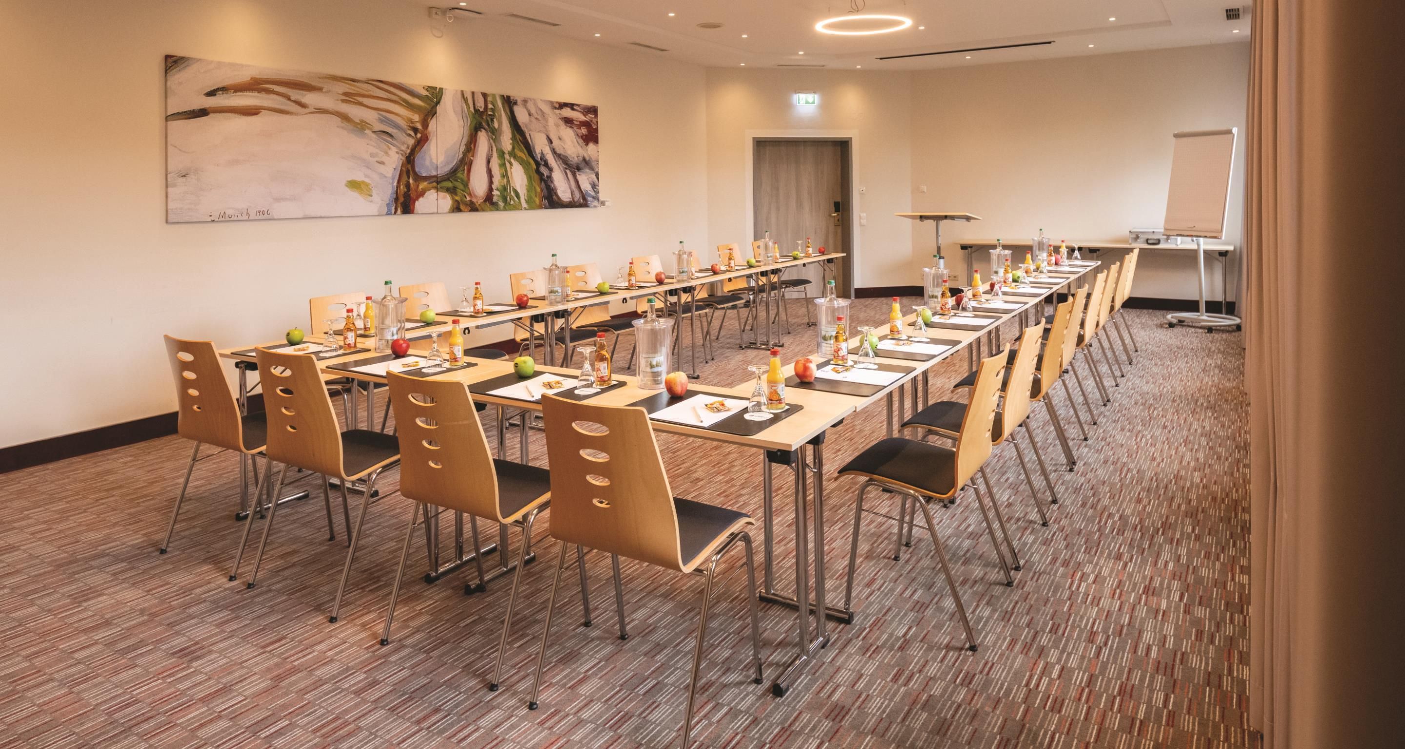 A conference room with a long table, chairs, and various items like bottles and fruits.