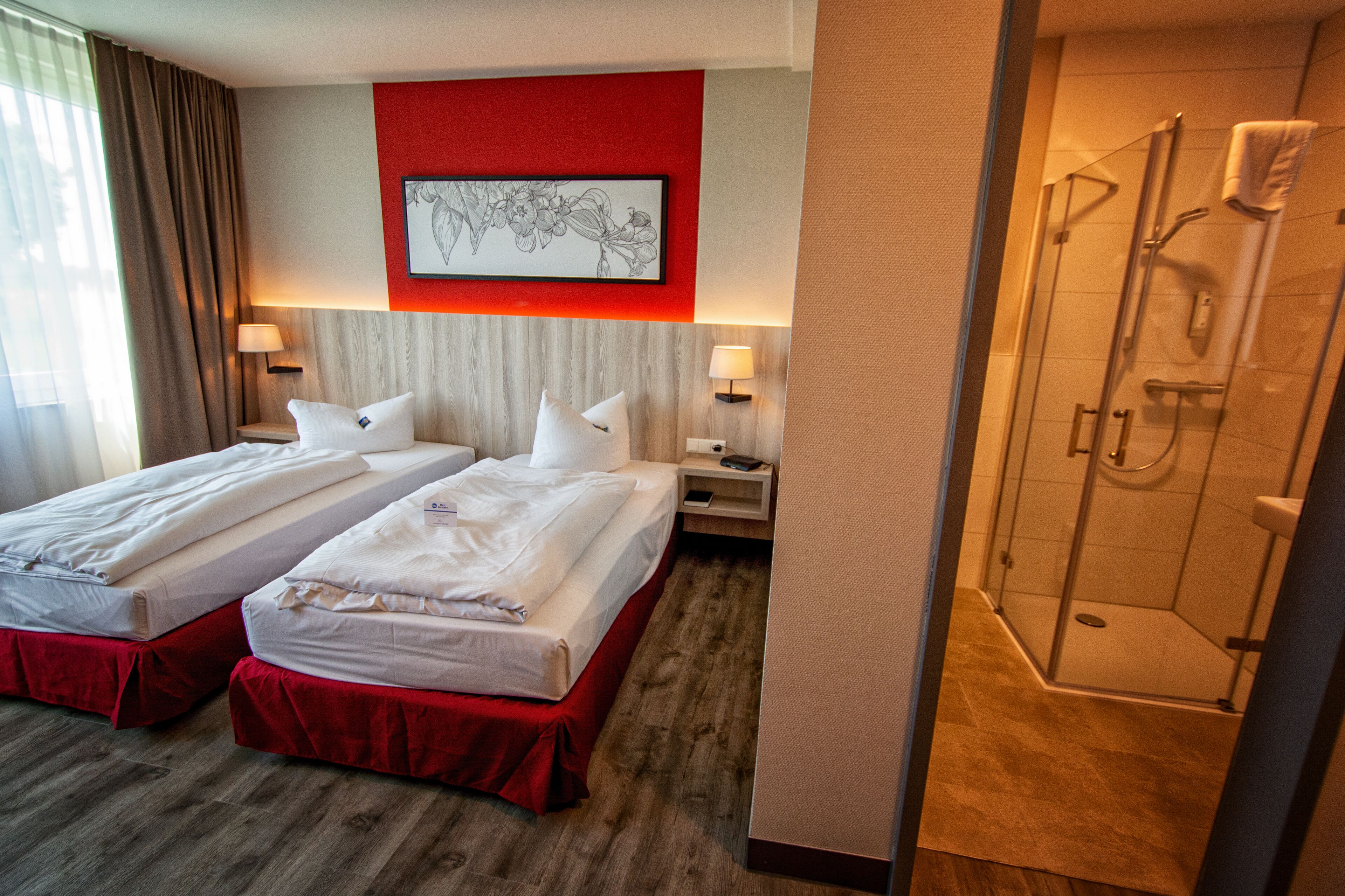 A hotel room with two beds, a shower, and a red accent wall.