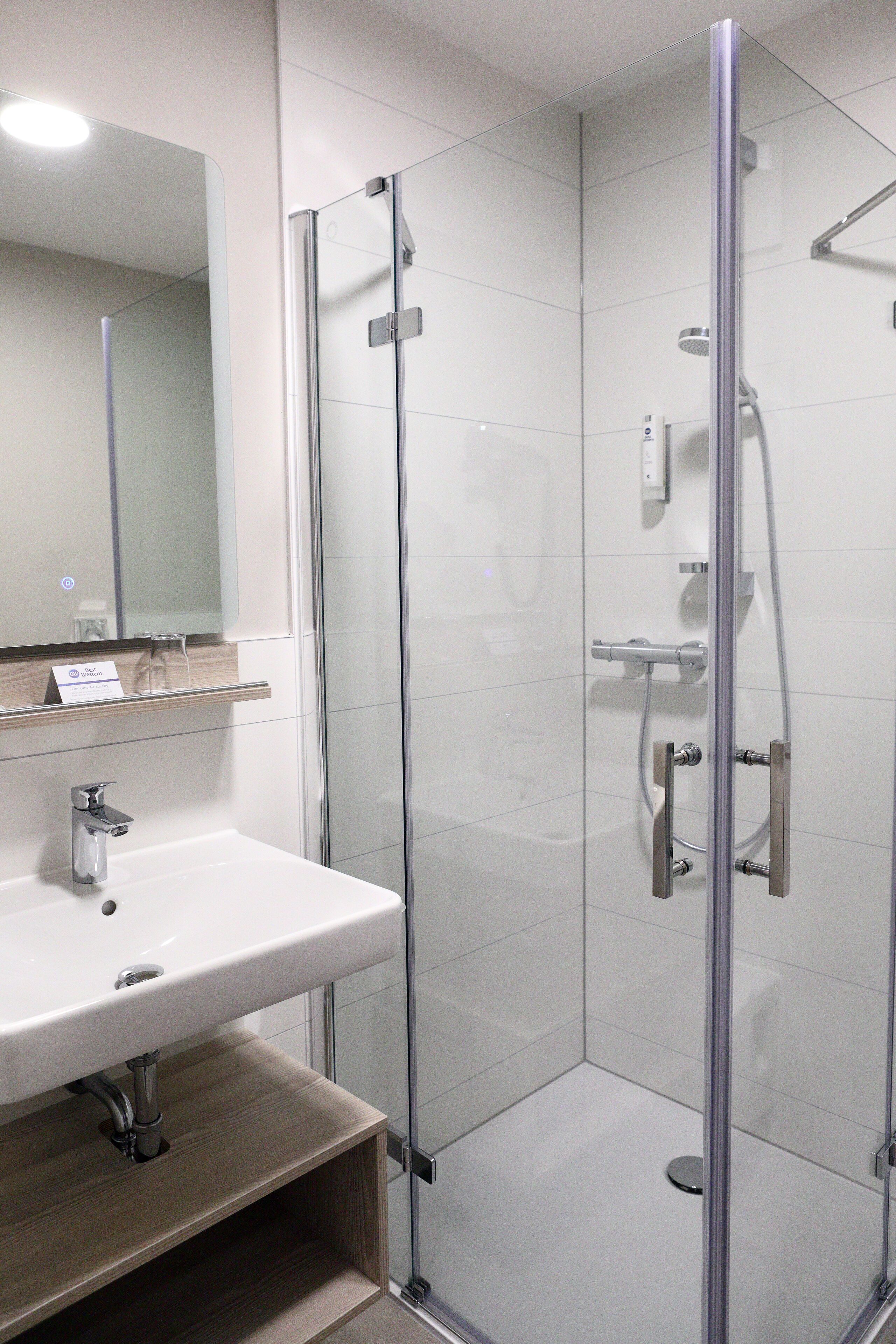 Un baño moderno con ducha de vidrio, lavamanos blanco y espejo sobre el lavamanos.