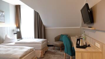 Ein Hotelzimmer mit zwei Betten, einem Schreibtisch mit Kaffeemaschine, einem Fernseher und einem Sessel.