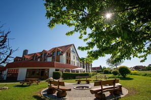 Un bâtiment avec un toit recouvert de tuiles rouges, de nombreuses fenêtres et une enseigne indiquant « Best Western ». On peut voir au premier plan des bancs en bois et un foyer extérieur.