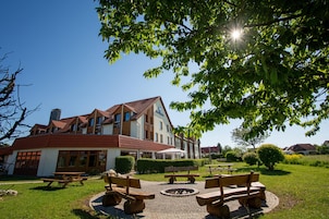 A building with a red-tiled roof, multiple windows, and a sign that reads 'Best Western.' There are outdoor wooden benches and a fire pit in the foreground.