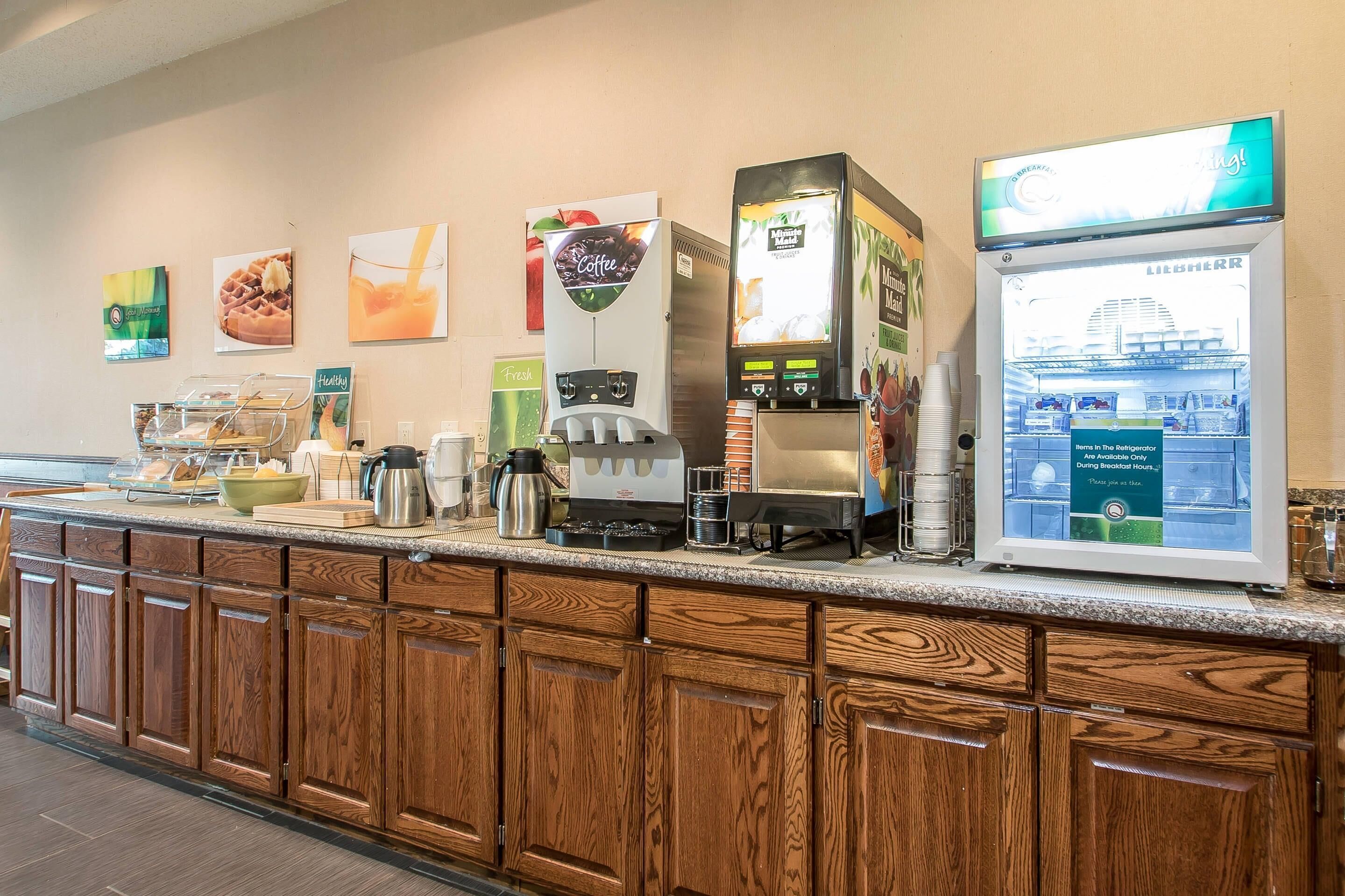 A breakfast bar with coffee machines, a refrigerator, and various food items.