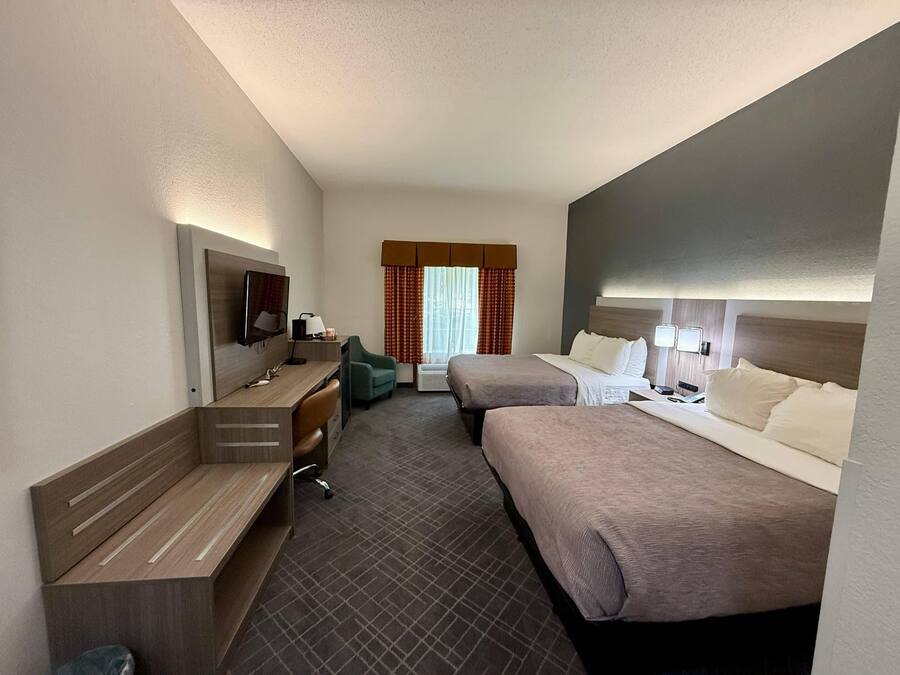 A hotel room with two beds, a desk with a chair, a television, and a window with curtains.