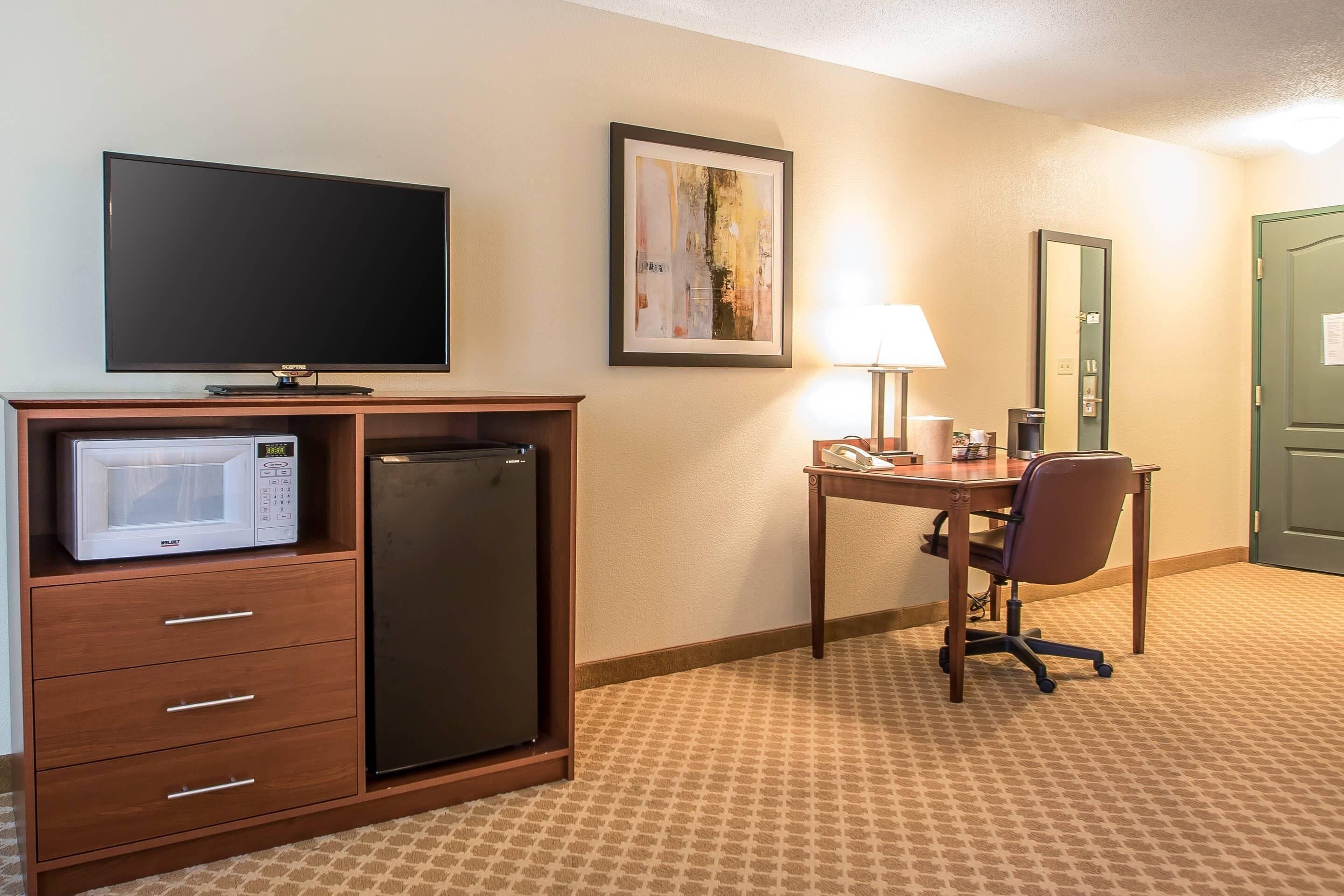 Habitación de hotel con televisión de pantalla plana, microondas, refrigerador, escritorio con silla, lámpara y puerta.