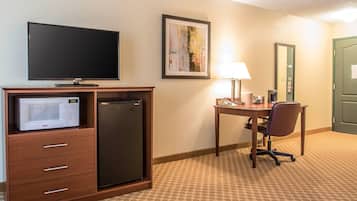 Habitación de hotel con televisión de pantalla plana, microondas, refrigerador, escritorio con silla, lámpara y puerta.