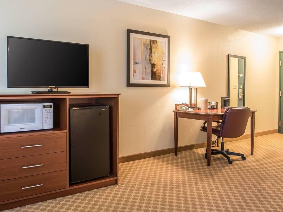 Une chambre d’hôtel équipée d’un téléviseur à écran plat, d’un four à micro-ondes, d’un réfrigérateur, d’un bureau avec une chaise, d’une lampe et d’une porte.
